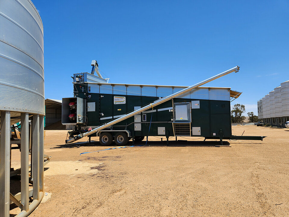 An Alvan Blanch grain dryer ina dirt yard. A silo sits to the left.